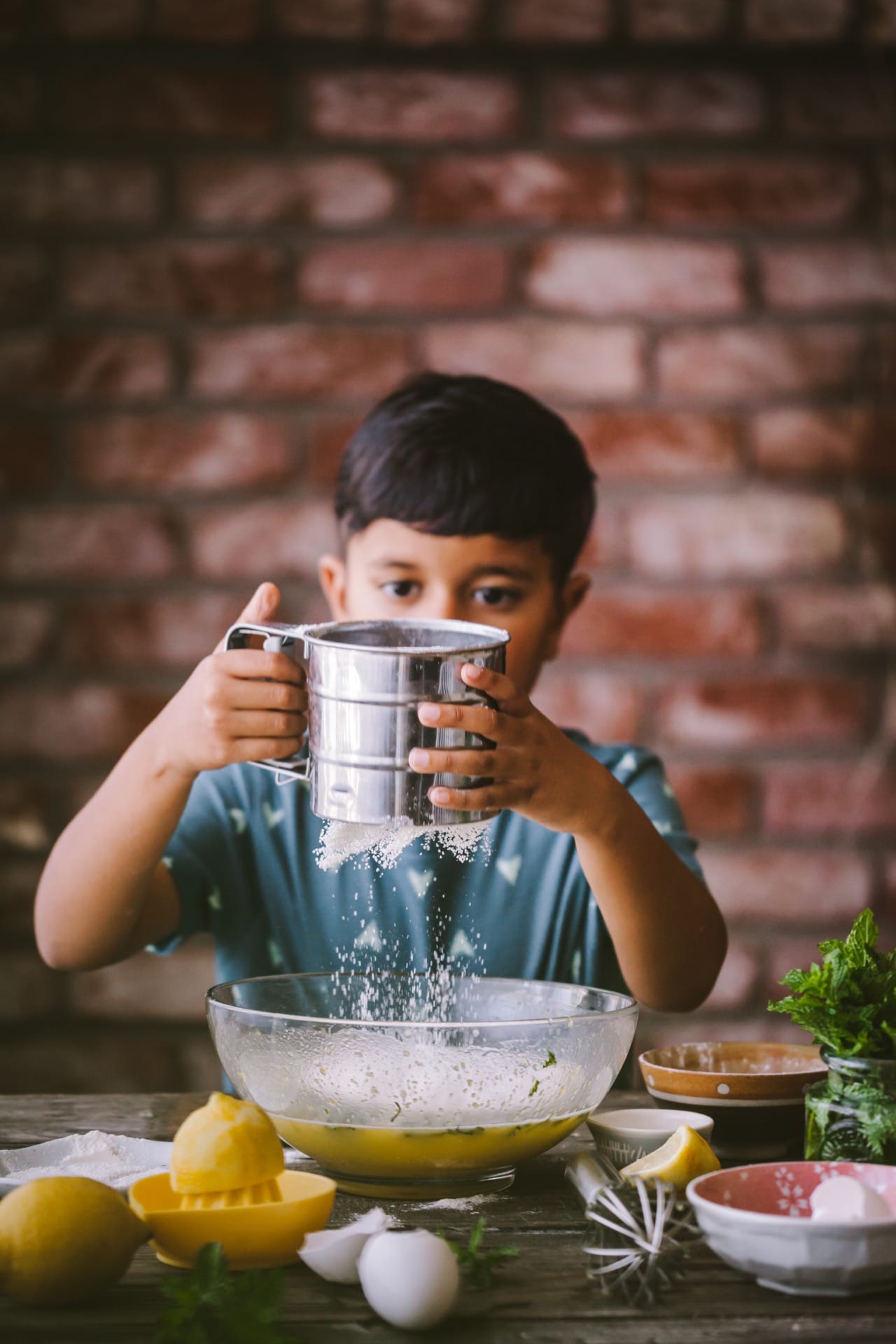 Little boy sifting flour to the cake mixing bowl