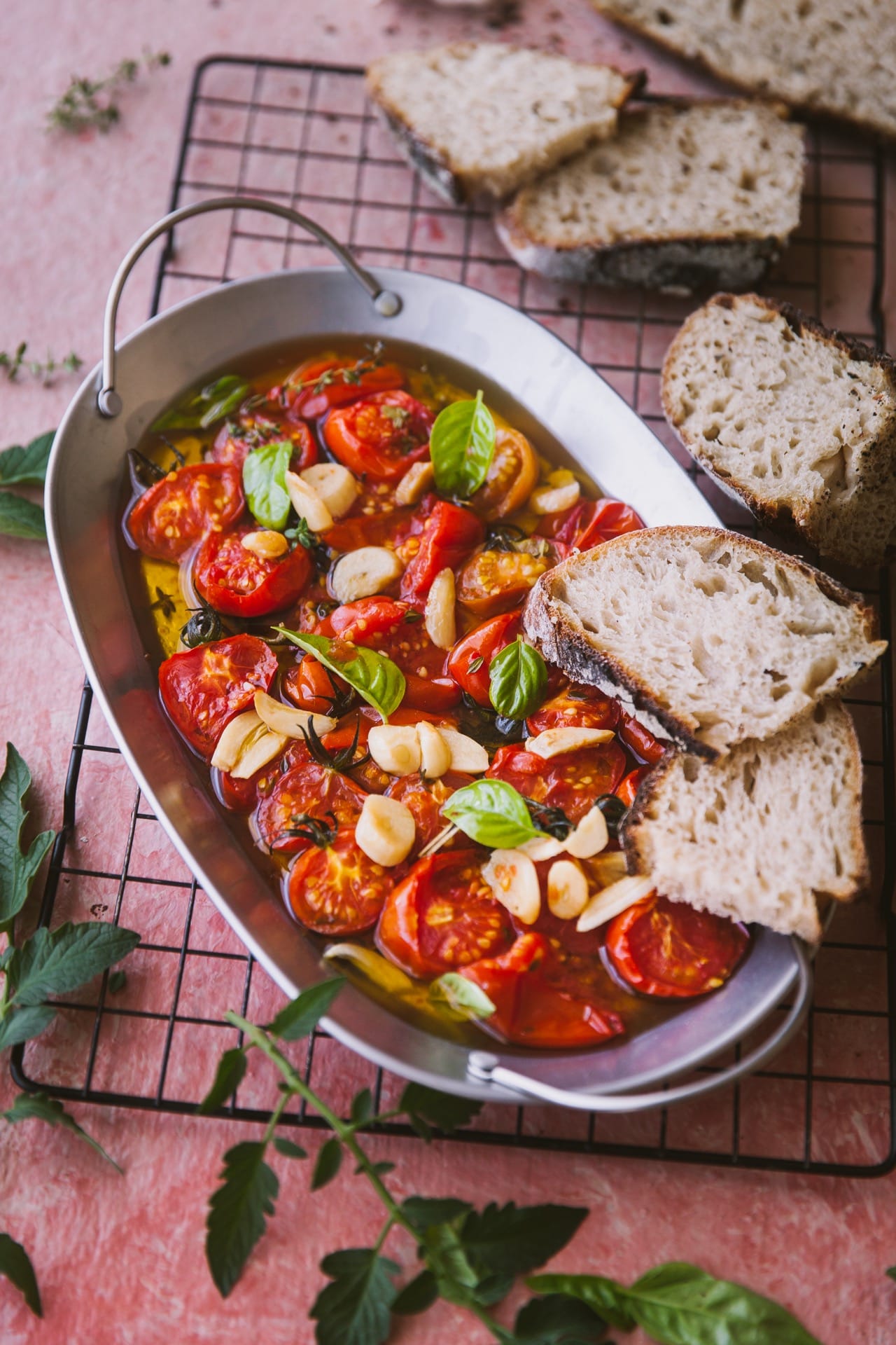 Tomato galic and basil on a tray with oil topped with two slices of bread and few bread slices are kept on the side