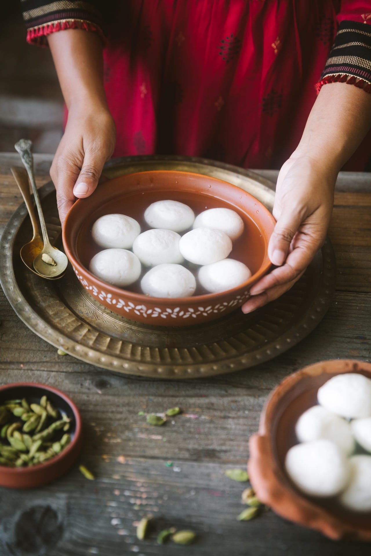 A bowl of rasgulla/ roshogolla with cardamom pods