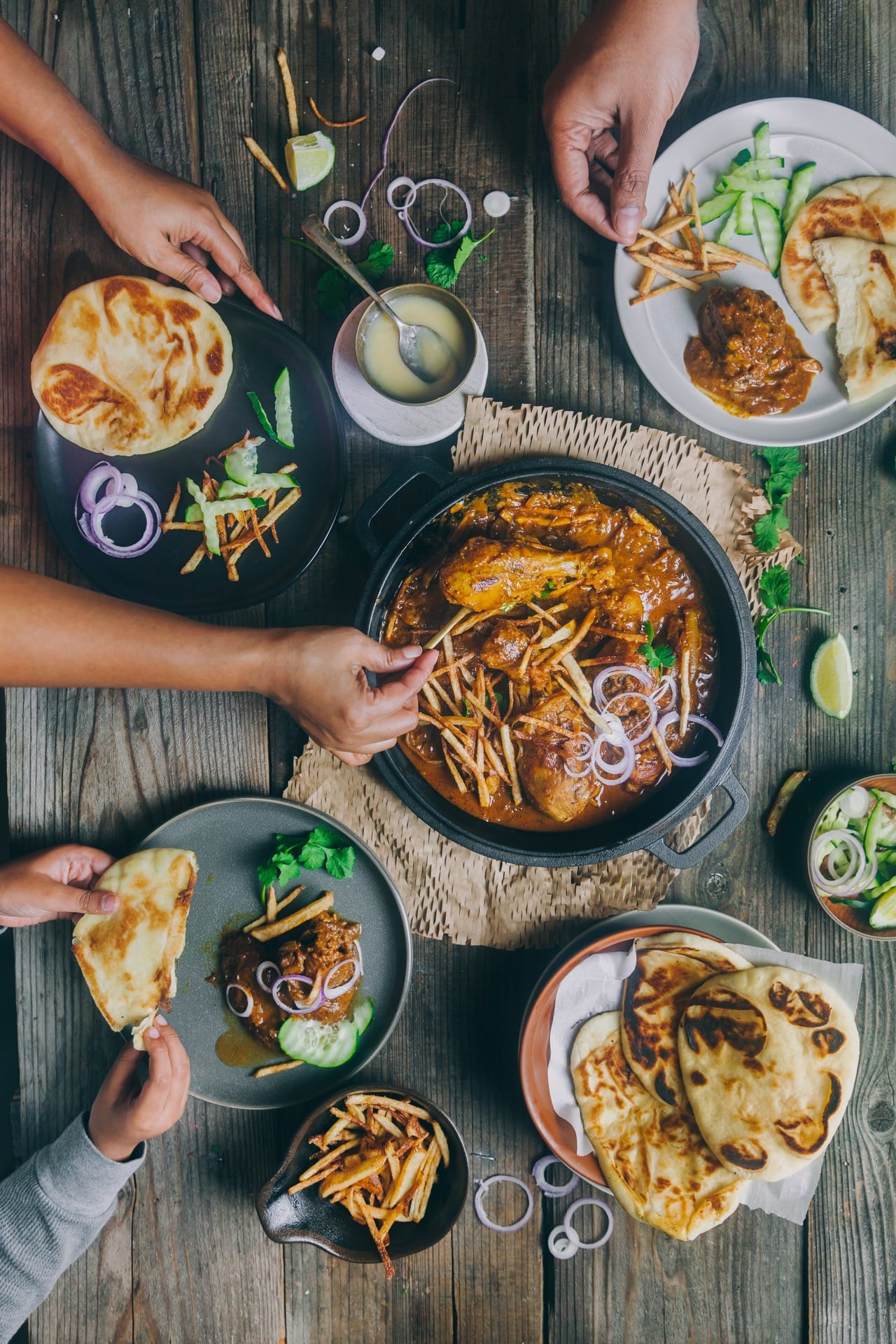 Flat lay view of Chicken Salli with plates across people eating