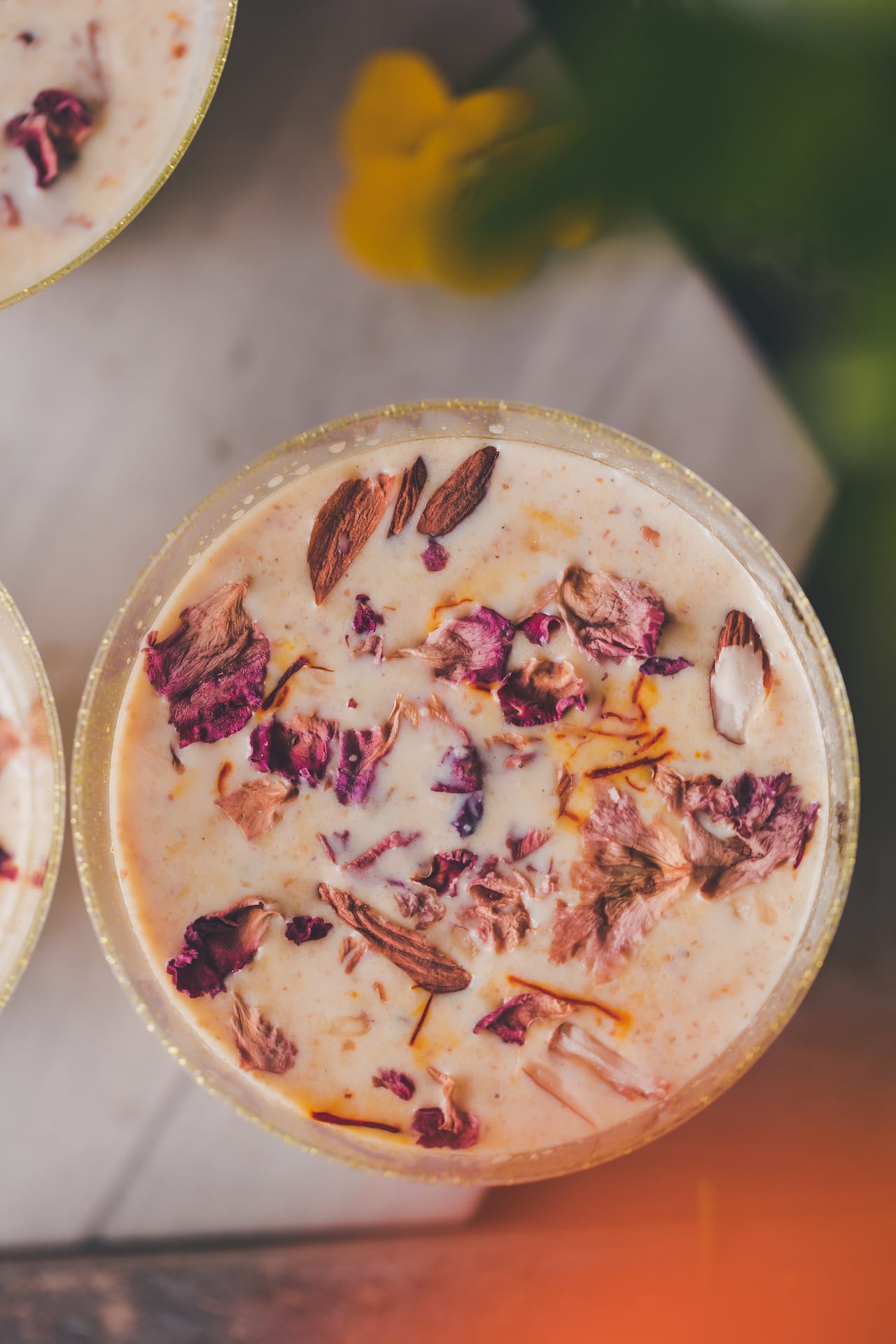 Close up photo of milk based Indian drink, garnished with rose petals and chopped nuts. 